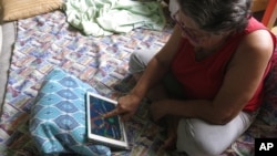 n this April, 5, 2017 photo, Mirna Lugo plays a game on her tablet to pass the time after dragging her mattress into the coolest part of her house because Puerto Rico's public power company cut the power in her neighborhood. 
