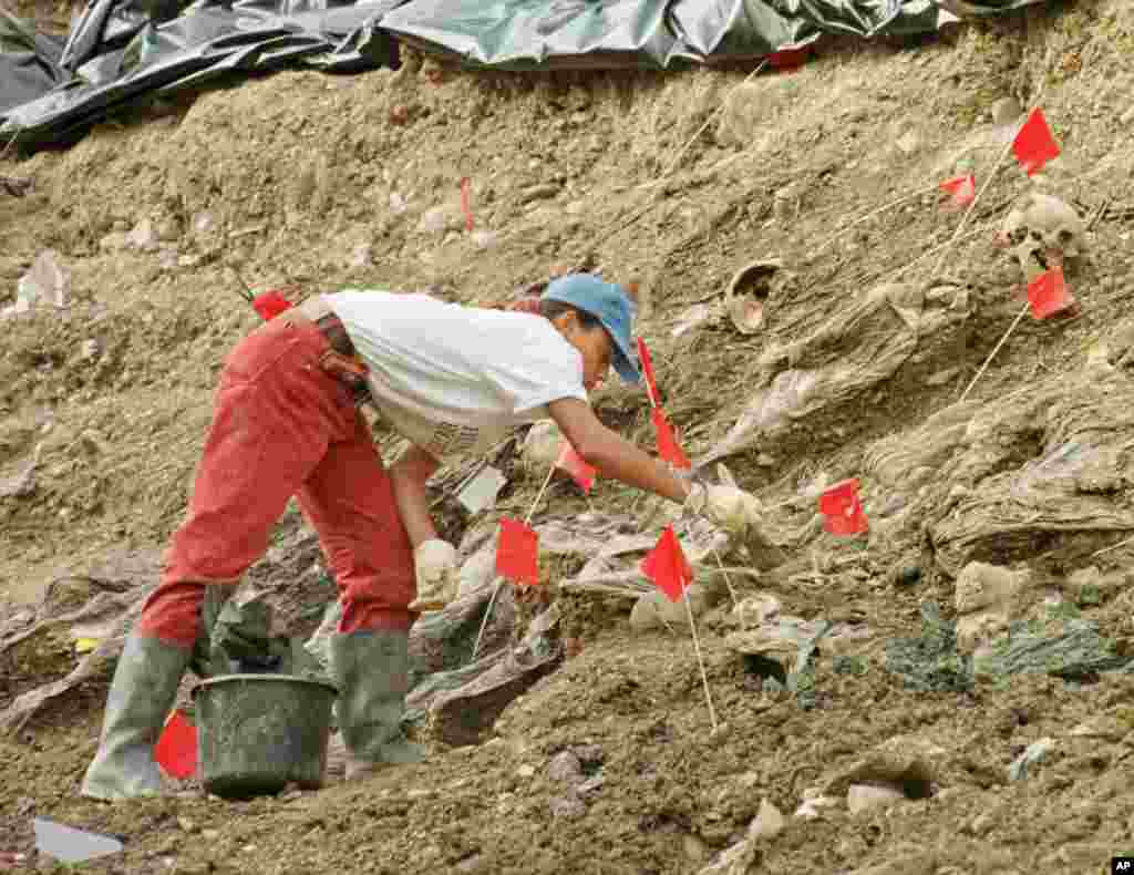 An international war crimes tribunal investigator carefully brushes away soil and debris as she works to unearth a jumble of bodies at a mass grave site near the village of Cerska, some 12 miles northeast of Srebrenica. (File 2006)