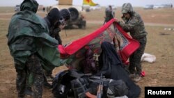 Members of the Syrian Democratic Forces help a woman near the village of Baghuz, in Deir el-Zour province, Syria, March 7, 2019.