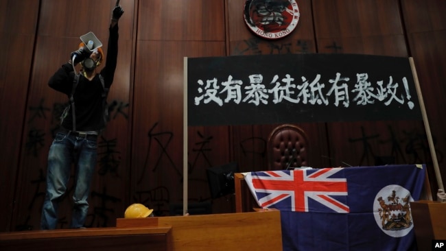 一名进入香港立法会的抗议者站在挂在立法会内的香港殖民地旗帜旁使用扩音喇叭讲话。(2019年7月1日)