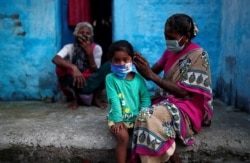 A woman wearing a protective face mask adjusts her daughter's face mask outside their house at a slum area, during an extended nationwide lockdown to slow the spreading of the coronavirus disease (COVID-19), in New Delhi, India, June 24, 2020