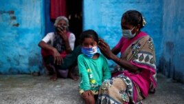 A woman wearing a protective face mask adjusts her daughter's face mask outside their house at a slum area, during an extended nationwide lockdown to slow the spreading of the coronavirus disease (COVID-19), in New Delhi, India, June 24, 2020