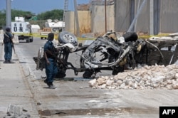 Somali soldiers pass near the wreckage of a car bomb outside the UN's office in Mogadishu on July 26, 2016.