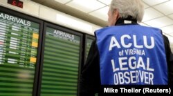 Seorang pengamat hukum American Civil Liberties Union mengawasi papan kedatangan penerbangan, ketika puluhan demonstran pro-imigrasi menyambut penumpang internasional yang tiba di Bandara Internasional Dulles, untuk memprotes perintah eksekutif Presiden D