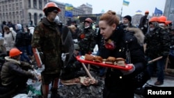 Seorang perempuan membawa sepiring sandwich saat demonatran anti-pemerintah Ukraina berkumpul di Lapangan Kemerdekaan (Independence Square) di pusat kota Kyiv (19/2).