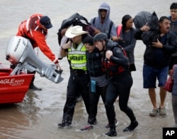 A woman is helped by rescue personnel while being evacuated as floodwaters from Tropical Storm Harvey rise Monday, Aug. 28, 2017, in Houston.