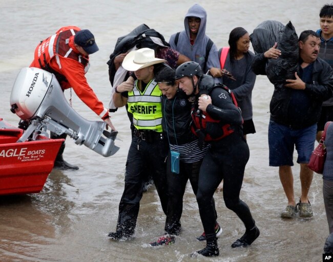 A woman is helped by rescue personnel while being evacuated as floodwaters from Tropical Storm Harvey rise Monday, Aug. 28, 2017, in Houston.