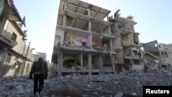 A fighter of Free Syrian Army's Tahrir al Sham brigade walks in front of building destroyed during yesterdays Syrian Air force air strike in Mleha suburb of Damascus January 21, 2013.