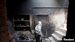 FILE - Azra looks at her dead pet bird in a cage at her home, which was burnt by a mob two days earlier, in Badami Bagh, Lahore, March 11, 2013.