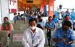 People wearing protective masks sit as they queue for their turn to receive a dose of the AstraZeneca coronavirus disease (COVID-19) vaccine during the mass vaccination program for transportations workers at Kampung Rambutan bus station in Jakarta, Indonesia