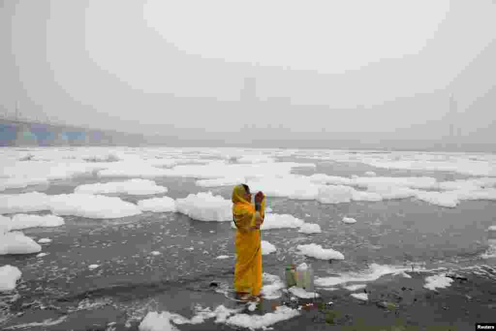 A woman prays on the side of the river Yamuna on a smoggy morning in New Delhi, India.