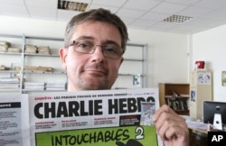 FILE - In this Sept.19, 2012 file photo, Stephane Charbonnier also known as Charb , the publishing director of the satyric weekly Charlie Hebdo, displays the front page of the newspaper as he poses for photographers in Paris.