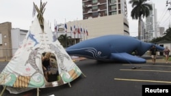 Para pengunjuk rasa mendirikan tenda tradisional (Teepee) bergambar paus dan lumba-lumba di dekat balon berbentuk paus, di depan gedung tempat pelaksanaan konferensi Komisi Ikan Paus Internasional (IWC) di kota Panama (4/7).