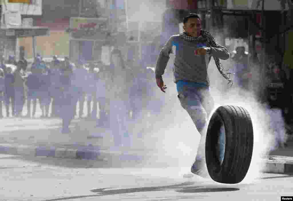 A Palestinian protester kicks a burning tire during clashes with Israeli troops following an anti-Israel demonstration in the West Bank city of Hebron, Nov. 14, 2014.