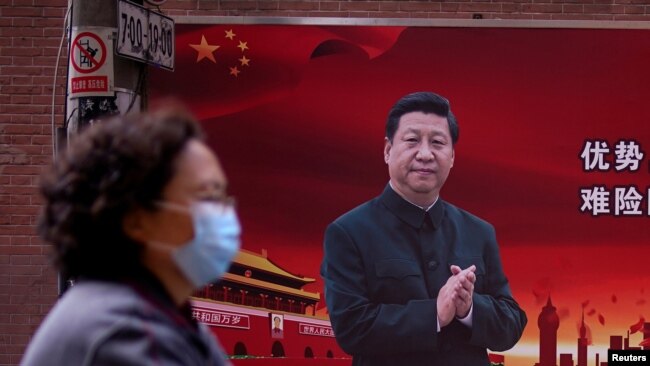 一位戴口罩的妇女从习近平的宣传画前走过（2020年3月12号）。