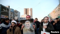 一名伊朗男子在伊朗高级将领苏莱曼尼的葬礼游行中手持苏莱曼尼的照片。（2020年1月6日）