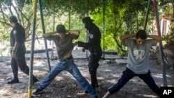 FILE - Two men are detained and searched by police in a park after a 911 call alerted police of possible gang members carrying assault rifles, in Ilopango, El Salvador, Aug. 31, 2015. 