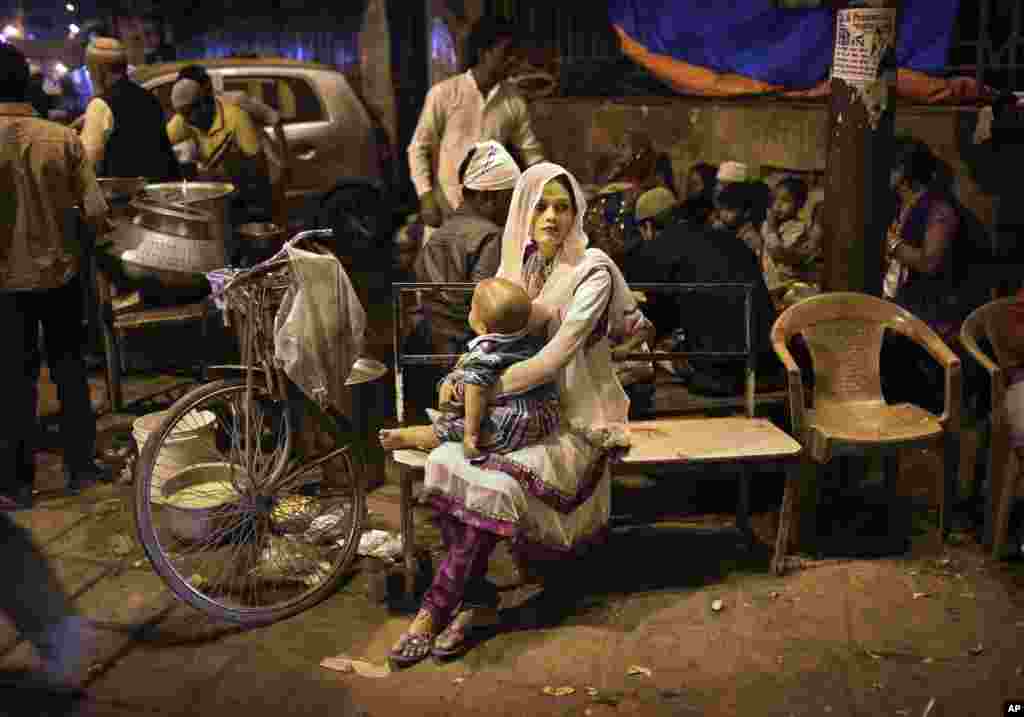An Indian Muslim woman holds her child as she waits on a bench at a food stall in New Delhi.