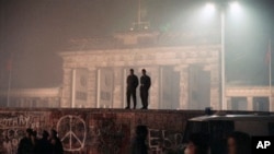 This was the scene when two East German border guards patrolled atop of Berlin Wall with the illuminated Brandenburg Gate in background, in Berlin, Nov. 14, 1989. (AP Photo/Jockel Finck)