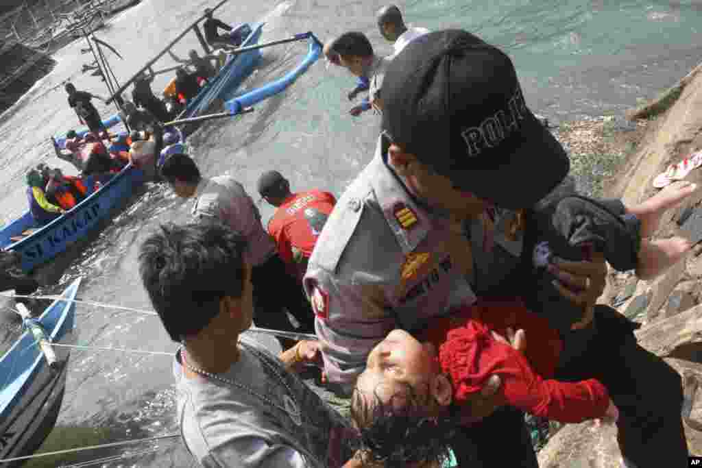 Seorang polisi membawa anak yang pingsan setelah kapal yang ditumpanginya terbalik di sebuah pantai di Jawa Barat (24/7).