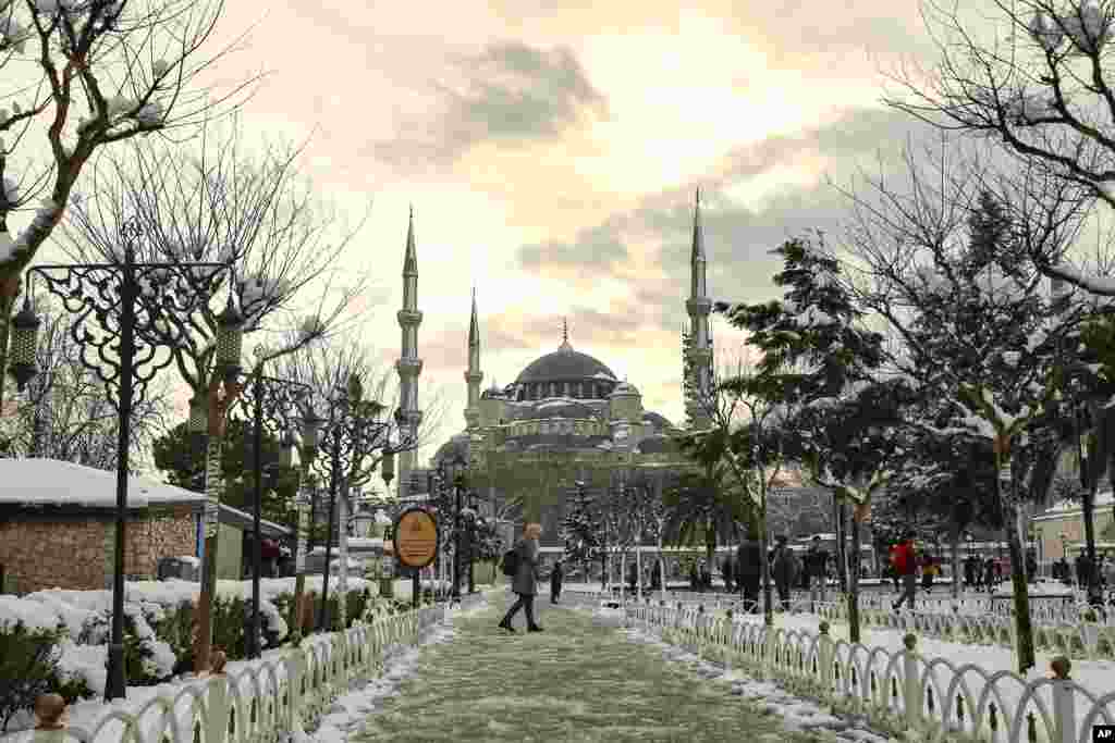 Orang-orang berjalan di taman tertutup salju dengan latar belakang Masjid Aya Sofia (Hagia Sophia) yang ikonik di Istanbul, Turki, Selasa (25/1). (Foto: AP)