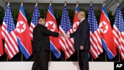 Le président américain Donald Trump tend la main au dirigeant nord-coréen Kim Jong Un à la station balnéaire de Capella sur l'île de Sentosa le mardi 12 juin 2018 à Singapour.