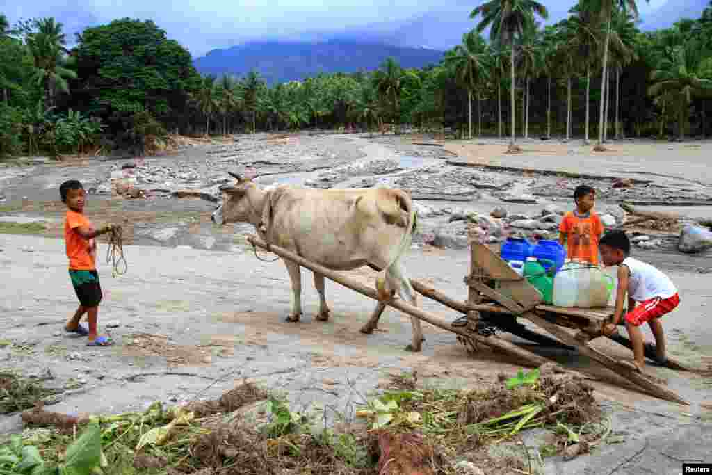 Anak-anak mengangkut jerigen-jerigen air minum yang ditarik sapi di desa yang hancur akibat banjir bandang di Pansor, Salvador, Lanao del Norte, Filipina selatan.