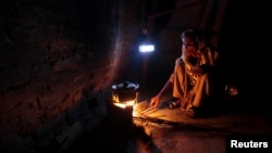 A woman cooks over a wood-burning fire under a battery-run emergency light during a power outage in a slum in Islamabad, Pakistan, Apr. 29, 2013. 