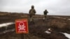 FILE - Ukrainian Military Forces servicemen walk past a metal plate which reads as 'Caution mines' on the frontline with Russia-backed separatists near Luganske village, in Donetsk region, Jan. 11, 2022.