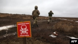FILE - Ukrainian Military Forces servicemen walk past a metal plate which reads as 'Caution mines' on the frontline with Russia-backed separatists near Luganske village, in Donetsk region, Jan. 11, 2022.