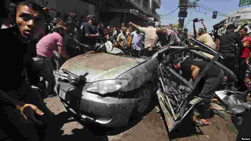 Palestinians gather around the remains of a car which police said was targeted in an Israeli air strike in Gaza City July 8, 2014.