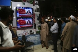 FILE - People listen a televised speech of Pakistani Prime Minister Imran Khan regarding his visit to Saudi Arabia, in Karachi, Pakistan, Oct. 24, 2018.