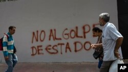 Varios ciudadanos caminan frente a un muro en Caracas en el que se puede leer un mensaje contrario al golpe de Estado.