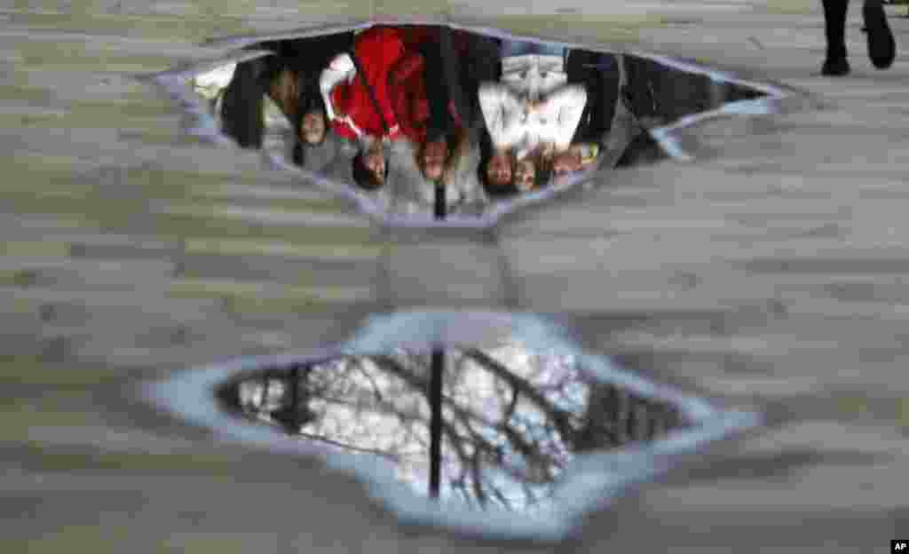 Pedastrians are reflected in a puddle in Westminster, London.