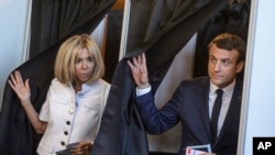 Tổng thống Pháp Emmanuel Macron (phải) và vợ ra khỏi phòng phiếu sau khi bỏ phiếu vòng đầu của 2 vòng bầu cử quốc hội Pháp.