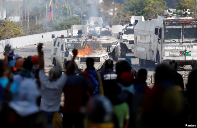 Opposition supporters react in front of a burning military vehicle during a rally against the government of Venezuela's President Nicolas Maduro in Caracas, Venezuela, May 1, 2019.