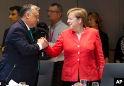 FILE - Hungarian Prime Minister Viktor Orban, left, greets German Chancellor Angela Merkel during a breakfast meeting at an EU summit in Brussels, Friday, June 29, 2018.