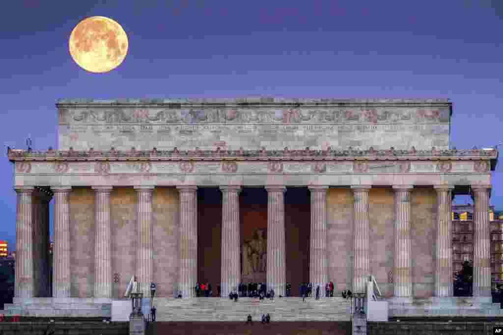 The full moon sets behind the Lincoln Memorial as people line the steps to watch the sun rise across the other end of the National Mall in Washington, March 31, 2018.