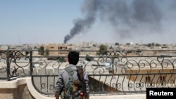 FILE - A Kurdish fighter from the People's Protection Units looks at smoke rising after a coalition airstrike in Raqqa, Syria, June 16, 2017. 