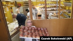 A worker carrying trays of paczki at a pastry shop for Fat Thursday in central Warsaw, Poland, Thursday, Feb. 4, 2016.