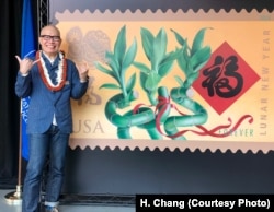 Kam Mak stands next to an image of the Year of the Dog stamp he created, which was dedicated in Honolulu. Mak is giving the friendly Hawaiian shaka sign, which means hang loose.