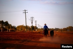 A stockman rides his horse as he leads another down a road toward the cattle yards in the outback town of Windorah, Queensland, located south of Stonehenge, in Australia, Aug. 11, 2017.