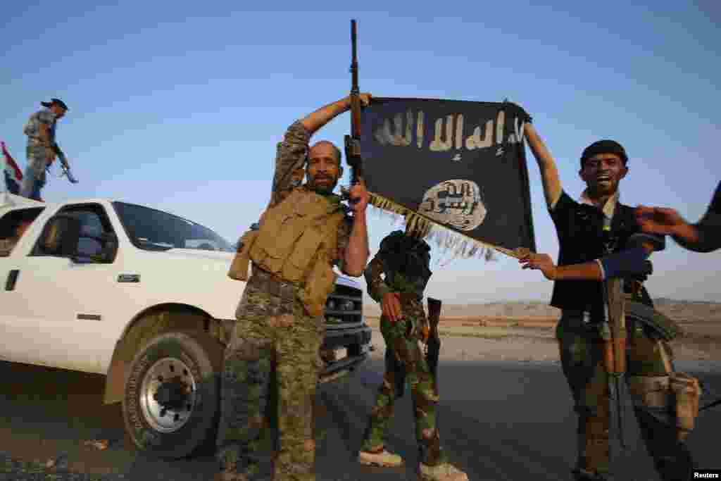 Pejuang milisi Syiah Irak memegang bendera ISIS untuk merayakan keberhasilan mereka memasuki kota Amerli yang dikepung oleh grup militan ISIS, 1 September 2014.
