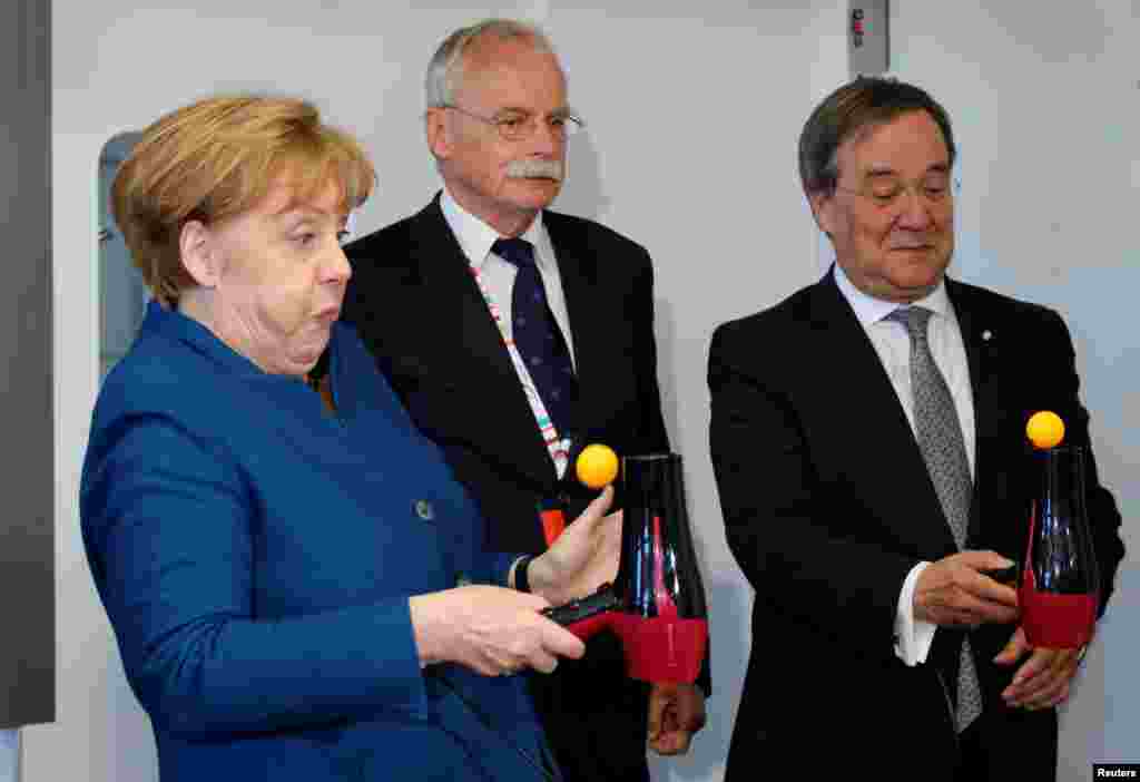 German Chancellor Angela Merkel reacts as she tests the so-called Bernoulli effect with a table tennis ball and a hair dryer, next to Ernst-Andreas Ziegler and Armin Laschet, federal Prime Minister of North Rhine-Westphalia, during her visit to the Junior University in Wuppertal.