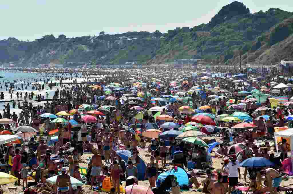 Beachgoers enjoy the sunshine as they sunbathe and play in the sea on Bournemouth beach in Bournemouth, southern England.