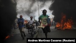 Para pengunjuk rasa berlari melewati ban-ban yang terbakar dalam demo menuntut pengunduran diri Presiden Haiti Jovenel Moise, di Port-au-Prince, Haiti, Rabu, 18 November 2020. (Foto:Andres Martinez Casares/Reuters))