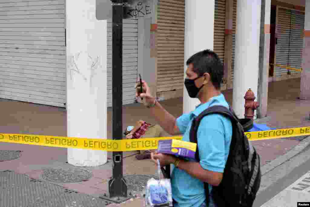 Un hombre que vende máscaras protectoras usa su teléfono móvil para tomar la foto del cadáver de un hombre que se había derrumbado en la acera, durante el brote de coronavirus, en Guayaquil.