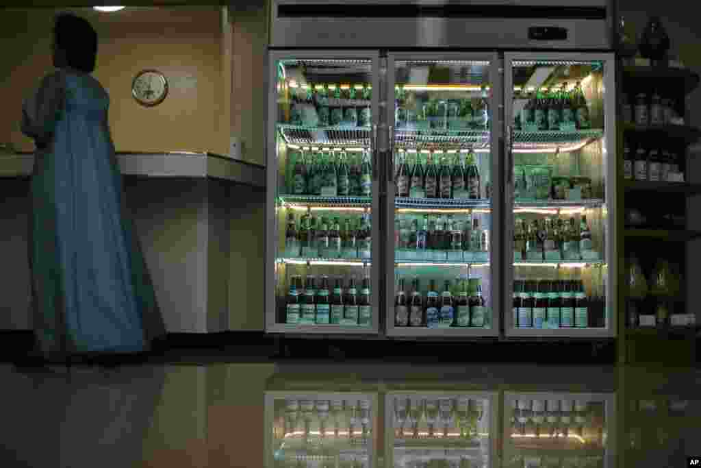 대동강맥주공장에서 생산한 다양한 맥주들을 진열한 냉장고 옆에 한복을 입은 안내원이 서 있다.
