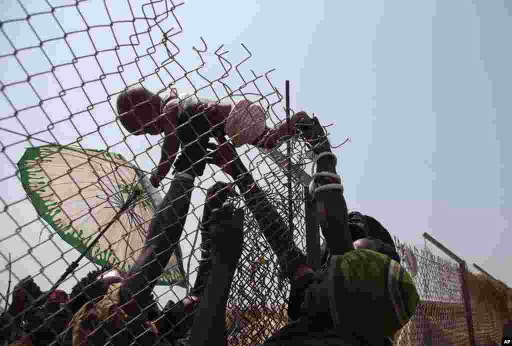 A baby is passed over a high fence surrounding an aid distribution point inside a makeshift camp at Mpoko Airport in Bangui, Jan. 8, 2014.