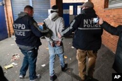 Police escort a handcuffed suspect to a police station during a raid operation in the Brooklyn borough of New York, January 4, 2022. (AP Photo/Seth Wenig)
